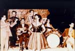 Πανηγύρι της Παναγιάς στην Αγιάσο το 1959. Στον "Κήπο της Παναγιάς" παίζουν οι Αγιασώτες μουσικοί, Βασίλης Σουσαμλής - βιολί, Στρατής Σουσαμλής - κλαρίνο, Γρηγόρης Κουρβανιός - κιθάρα, Παναγιώτης Μαλούκης - ακορντεόν, Παναγιώτης Π. Σουσαμλής - ντραμς, Ευριπίδης Ζαφειρίου ("Καζίνο") - σαξόφωνο, με την τραγουδίστρια Στέλλα Κοζαδίνου (;). Αρχείο Π. Σουσαμλή.
